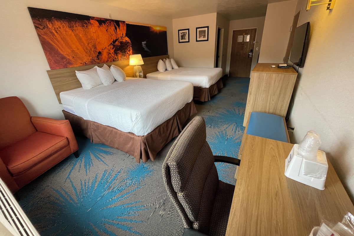 Ein Hotelzimmer mit zwei Betten, einem Schreibtisch, einem Sessel, einem Fernseher und einem Bild an der Wand.