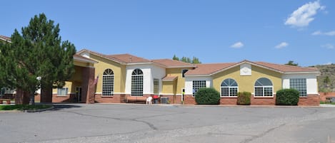 A two-story building with a yellow facade and red-tiled roof, featuring large arched windows and a central entrance.