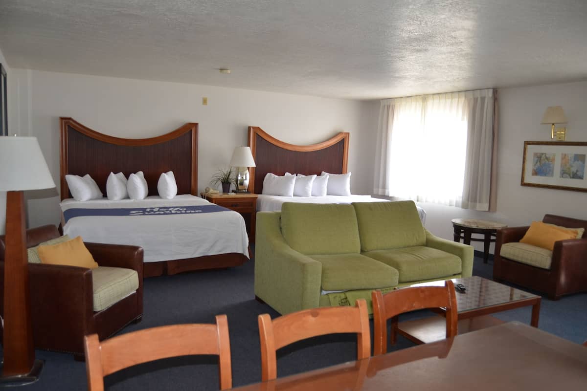 Ein Hotelzimmer mit zwei Betten, einem grünen Sofa, Holzstühlen, einem kleinen Tisch und einer Lampe.