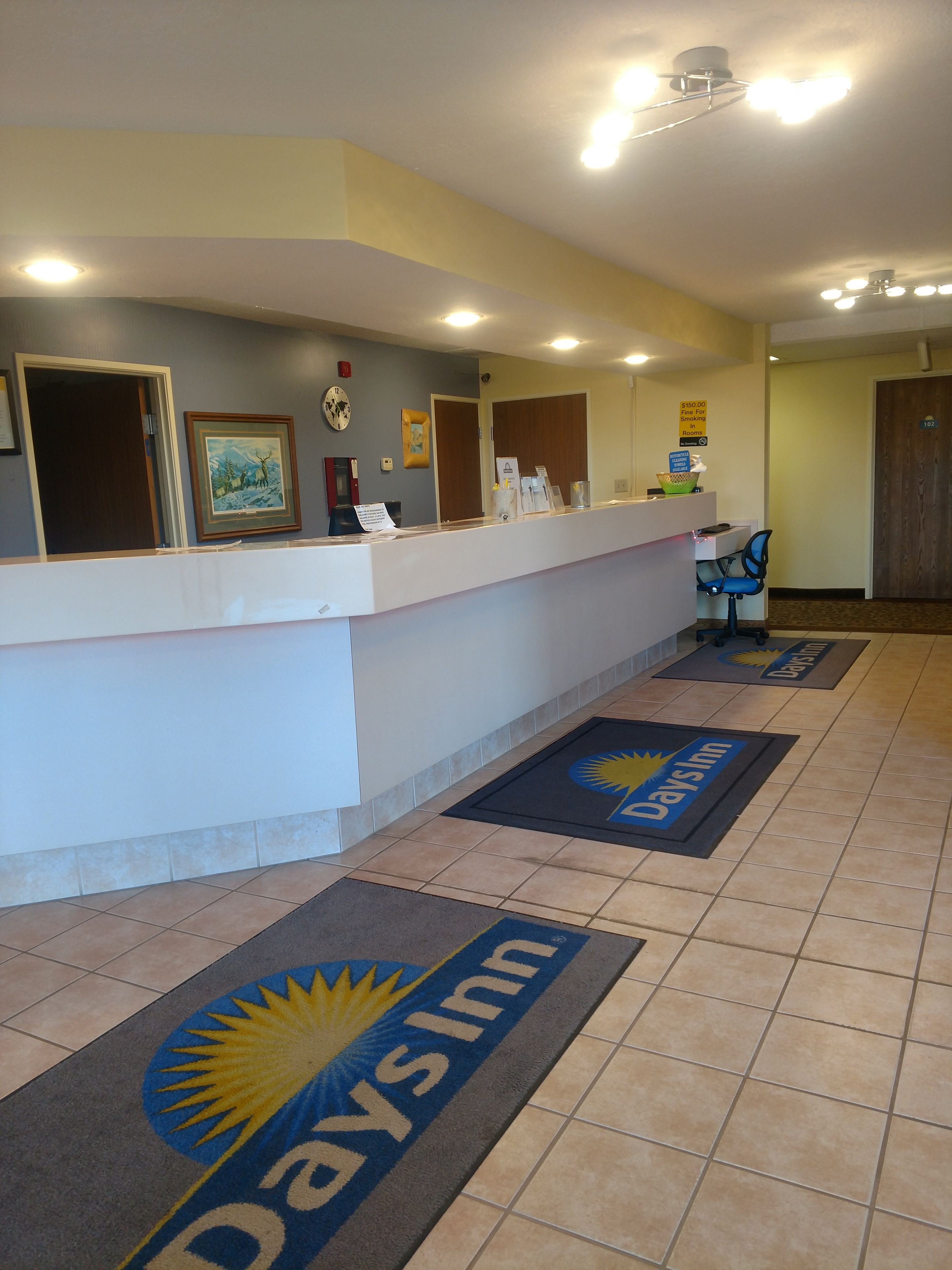 A reception area with a counter, framed pictures, a clock, and a sign indicating a $150.00 fine for smoking rooms.
