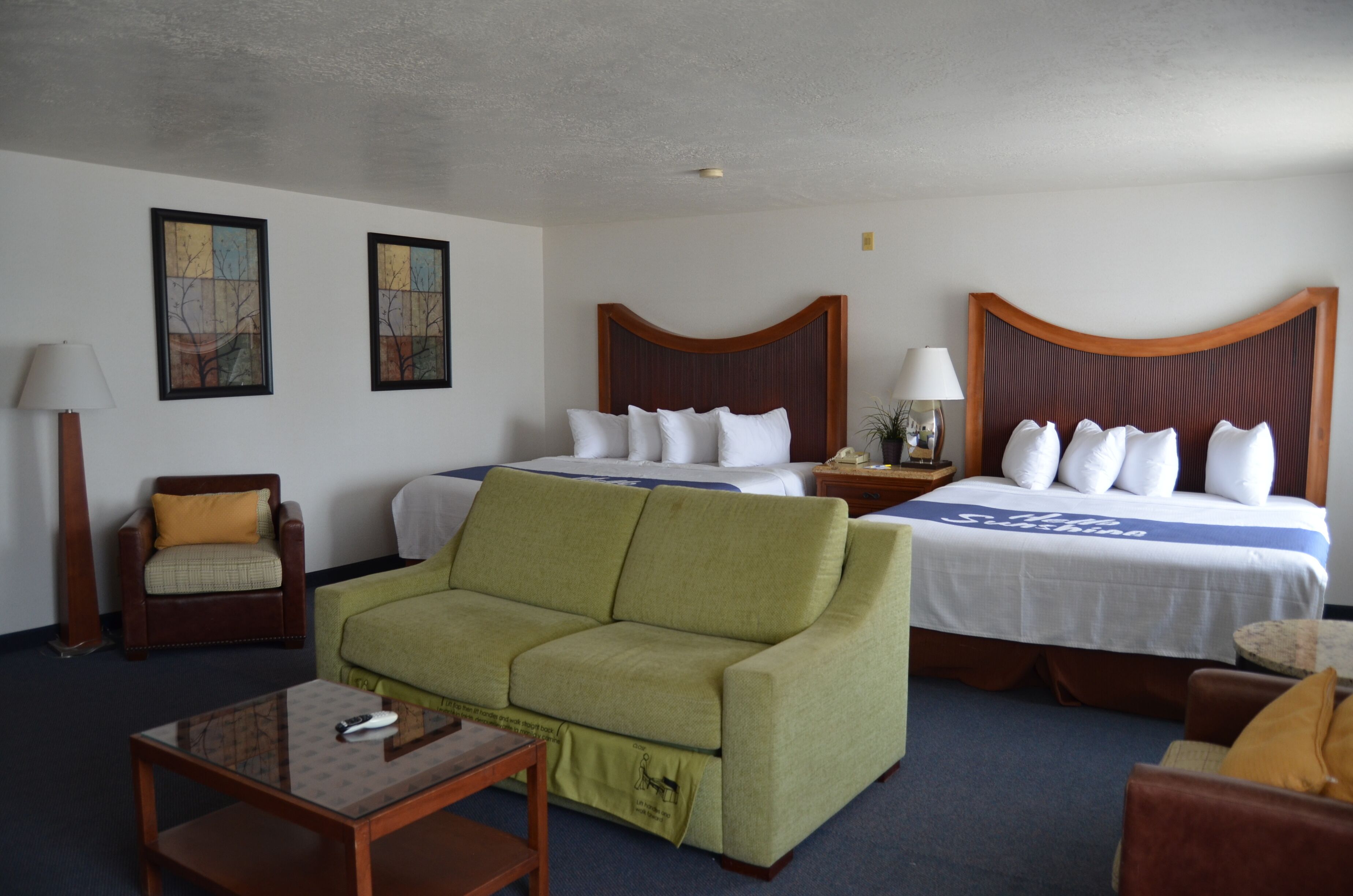 A hotel room with a bed, a green sofa, a wooden armchair, a small table, and two bedside tables with lamps.