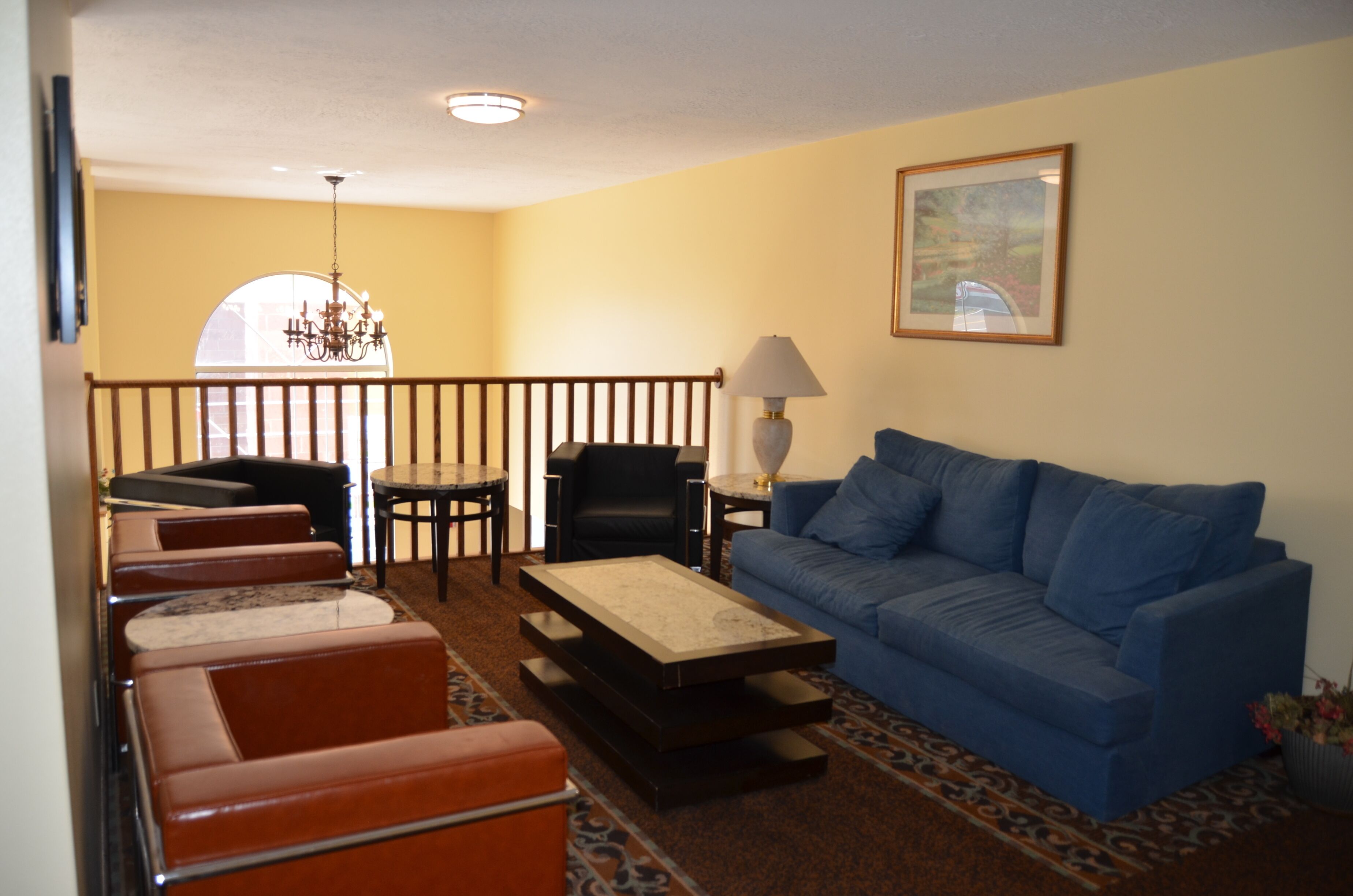 A living room with a blue sofa, brown leather chairs, a coffee table, a chandelier, and a painting on the wall.