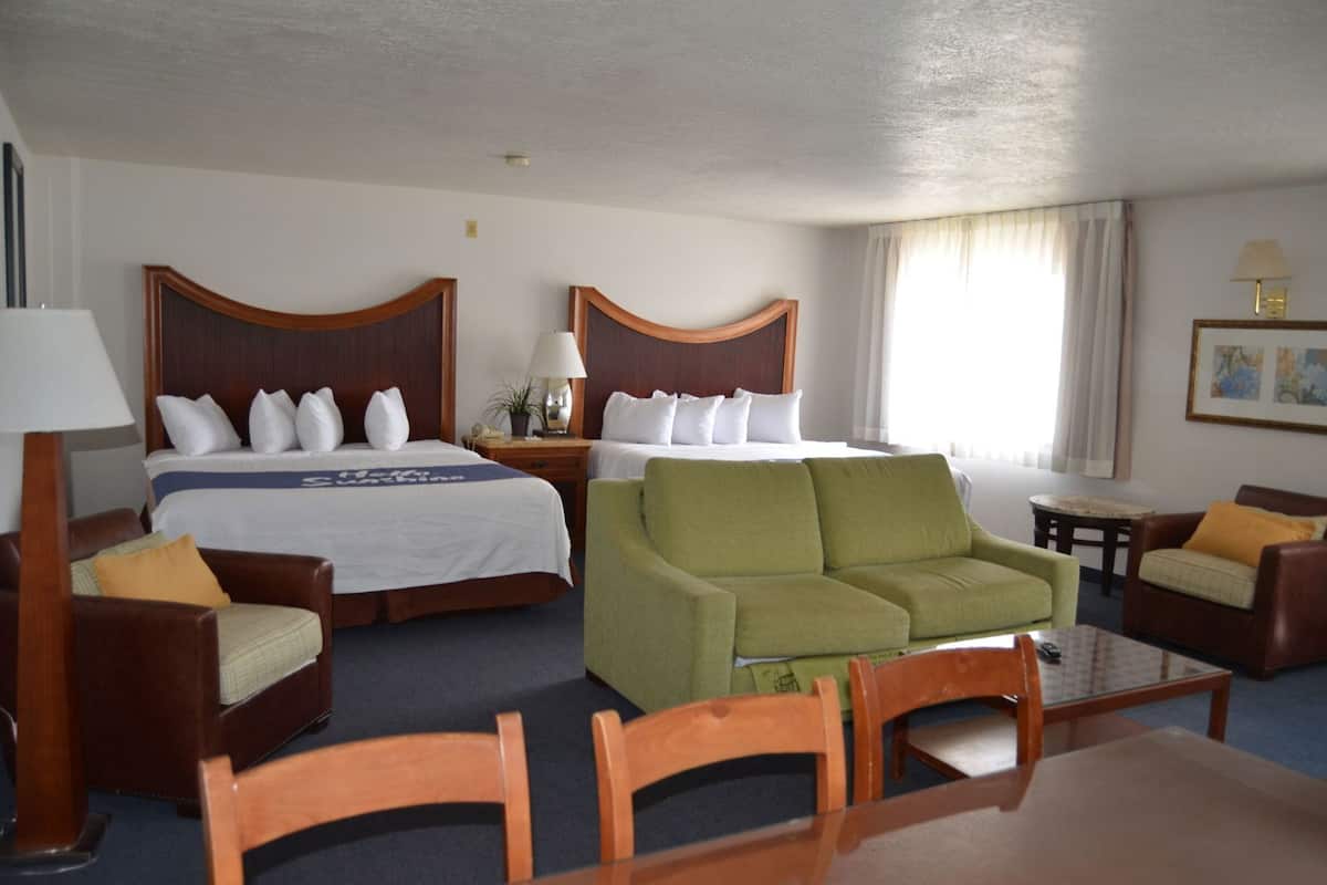 Ein Hotelzimmer mit zwei Betten, einem grünen Sofa, einem Holztisch und einem kleinen Nachttisch.