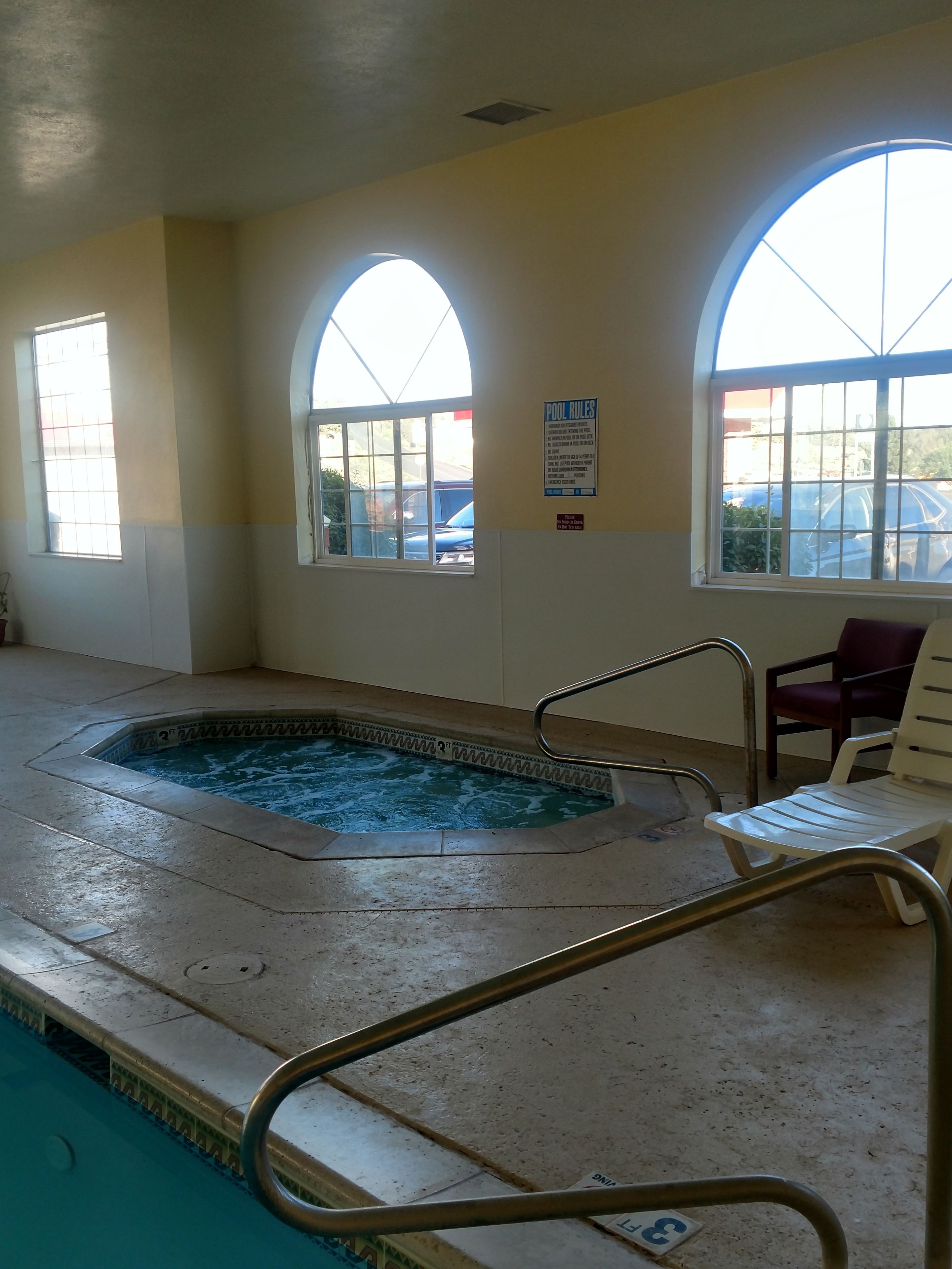 An indoor swimming pool with clear water, a metal ladder, and two arched windows.