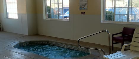 An indoor swimming pool with clear water, a metal ladder, and two arched windows.