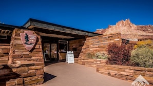 The entrance to a visitor center with a stone facade, a sign for the Geology Program, and a backdrop of a natural rock formation.
