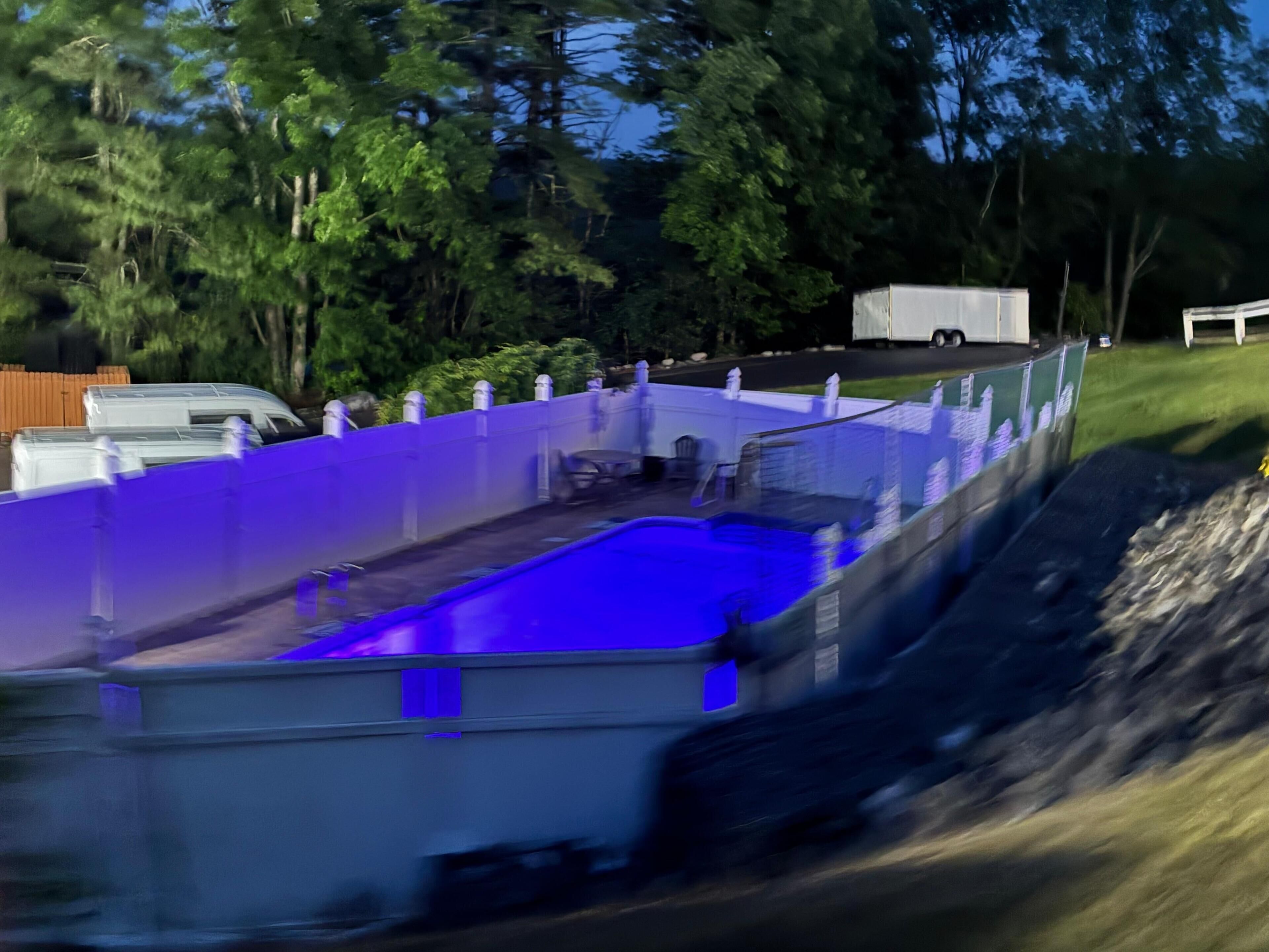 A swimming pool with a blue tint, surrounded by a white fence, and a truck parked nearby.