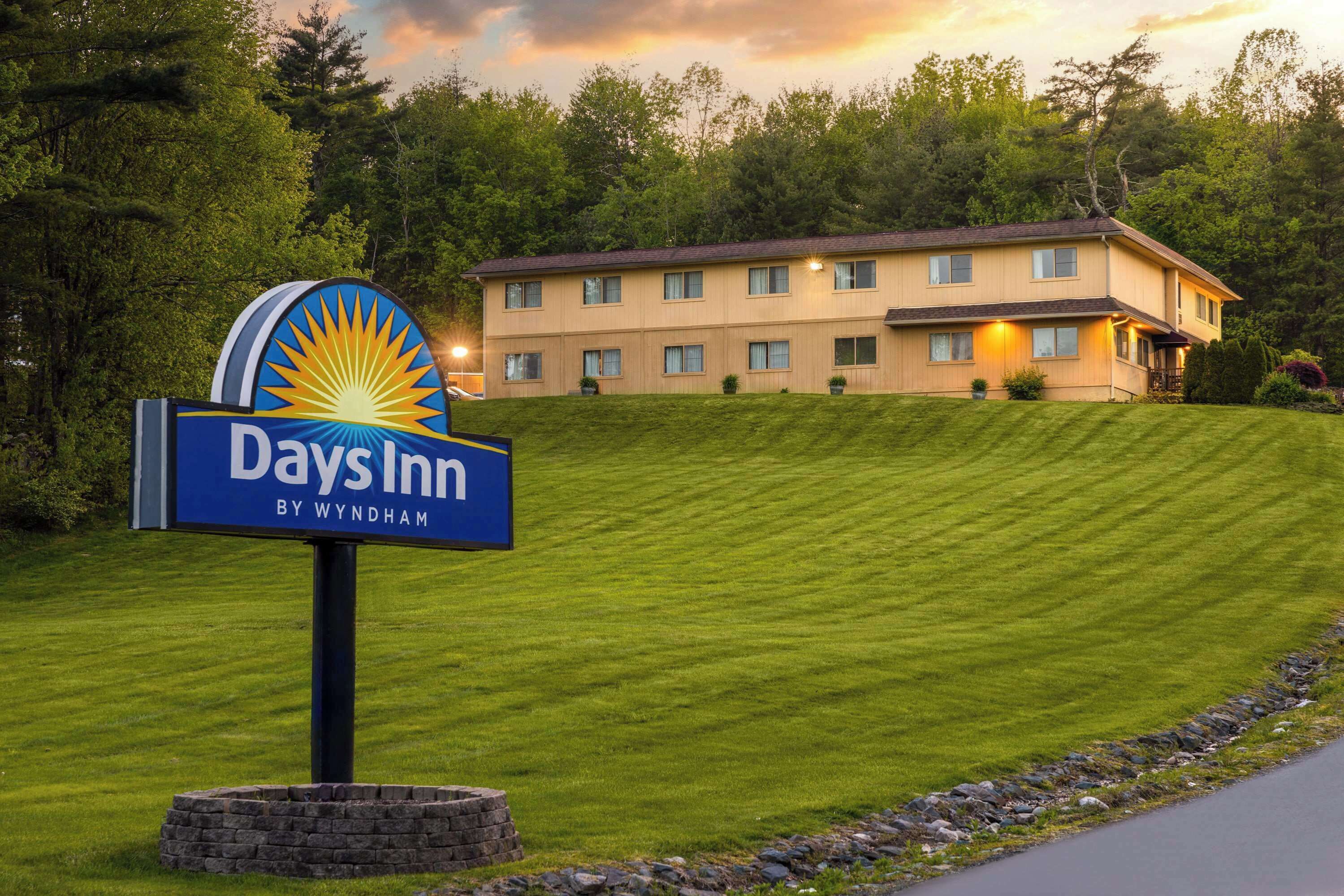 A Days Inn sign with a sun logo, a two-story building, and a well-maintained lawn.
