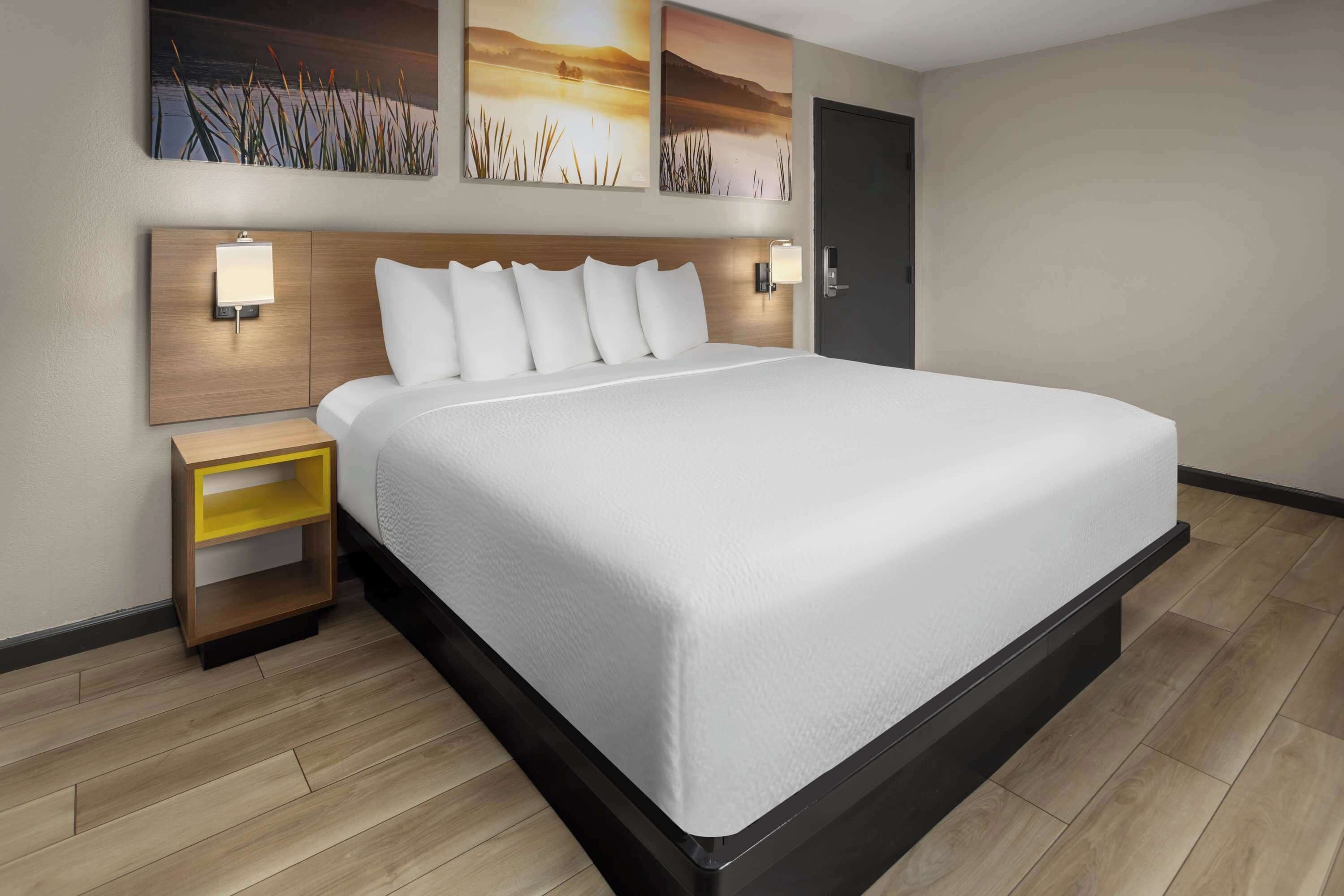 Una habitación de hotel con una cama grande, cabecera de madera, mesitas de noche y lámparas fijadas a la pared.
