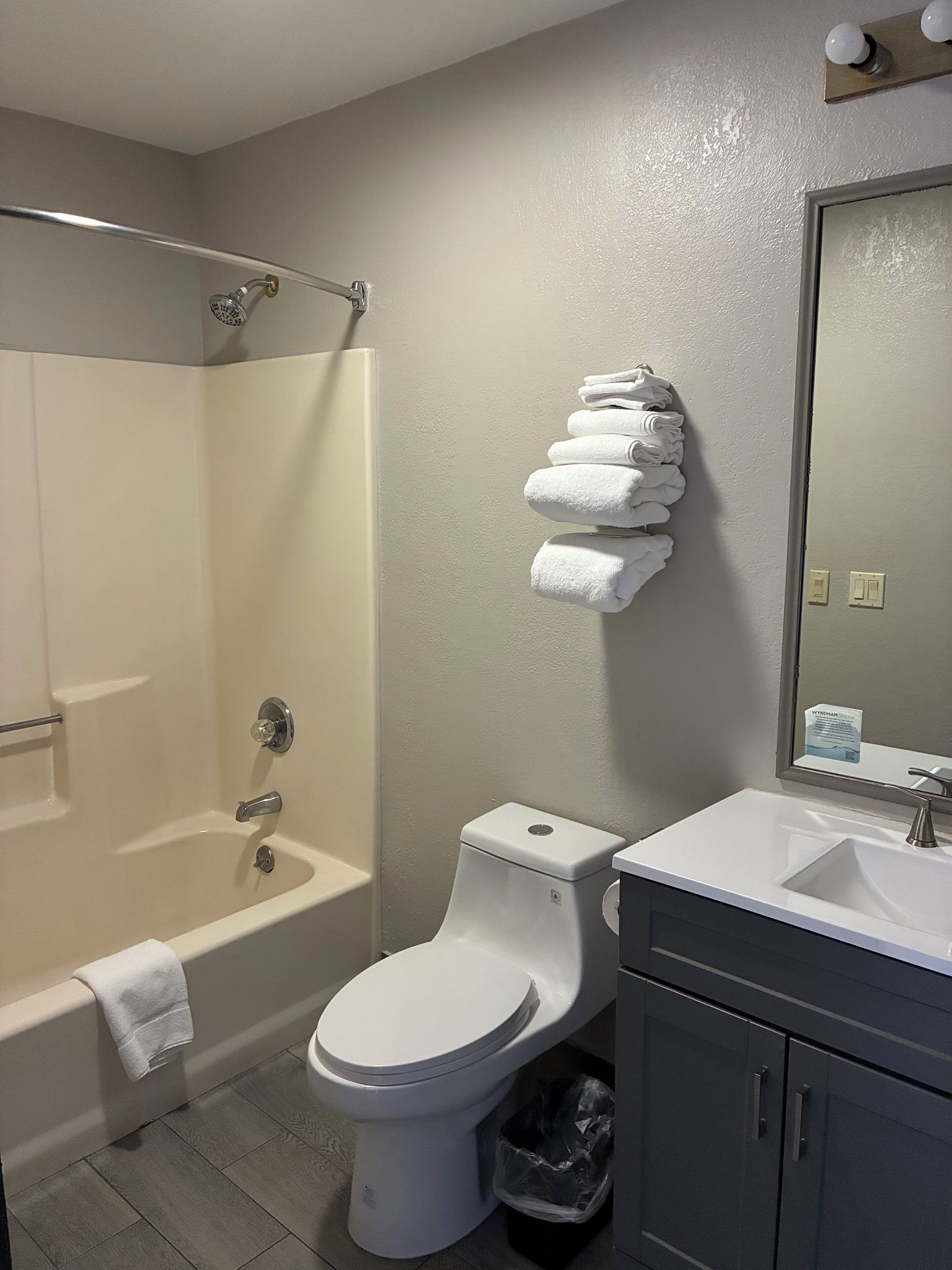 Een badkamer met een douche, toilet, wastafel en een stapel handdoeken aan de wand.