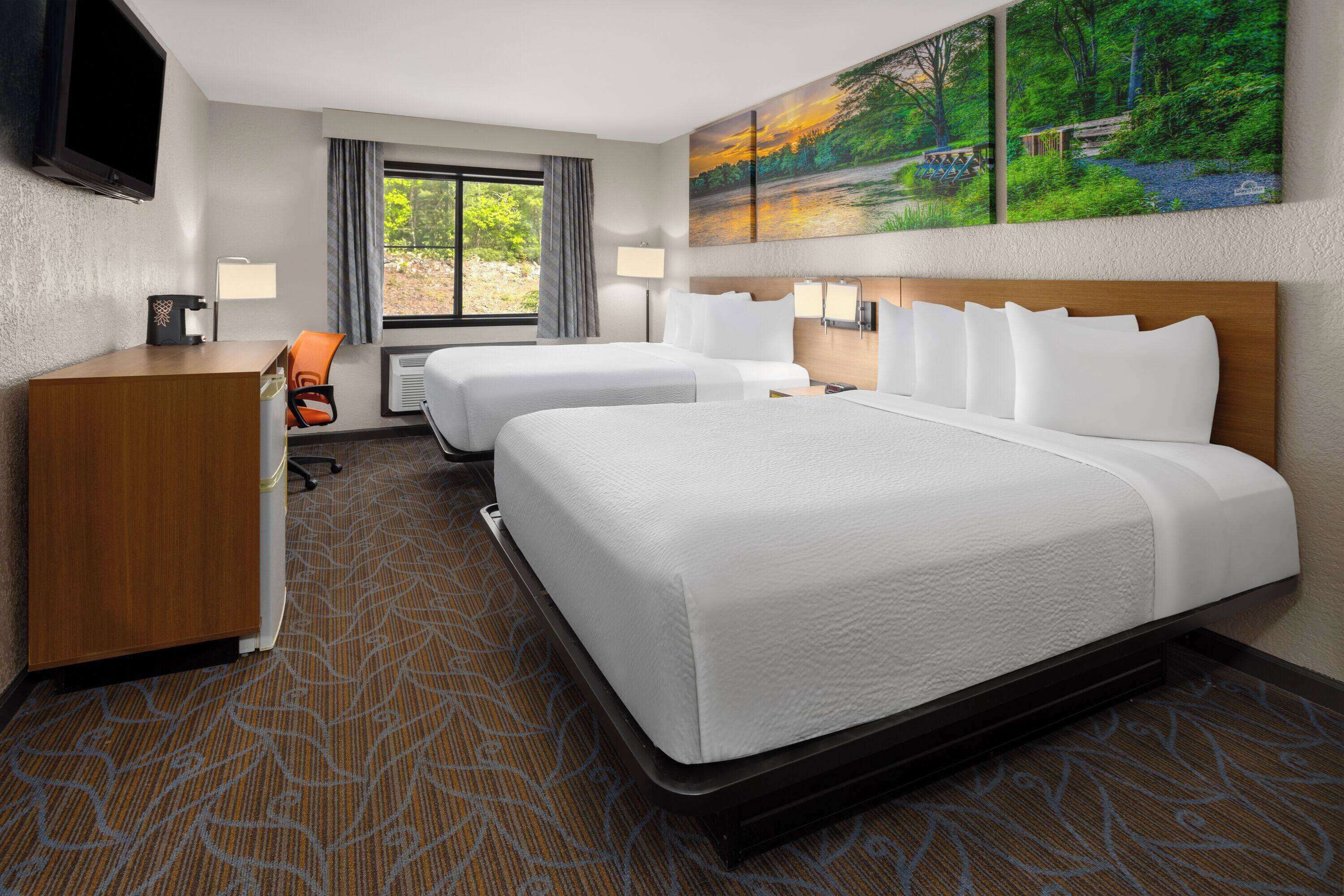 A hotel room with two beds, a desk, a chair, a TV, and a window with curtains.