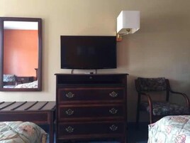 A hotel room with a bed, a dresser with drawers, a television on top of the dresser, a chair, and a mirror on the wall.