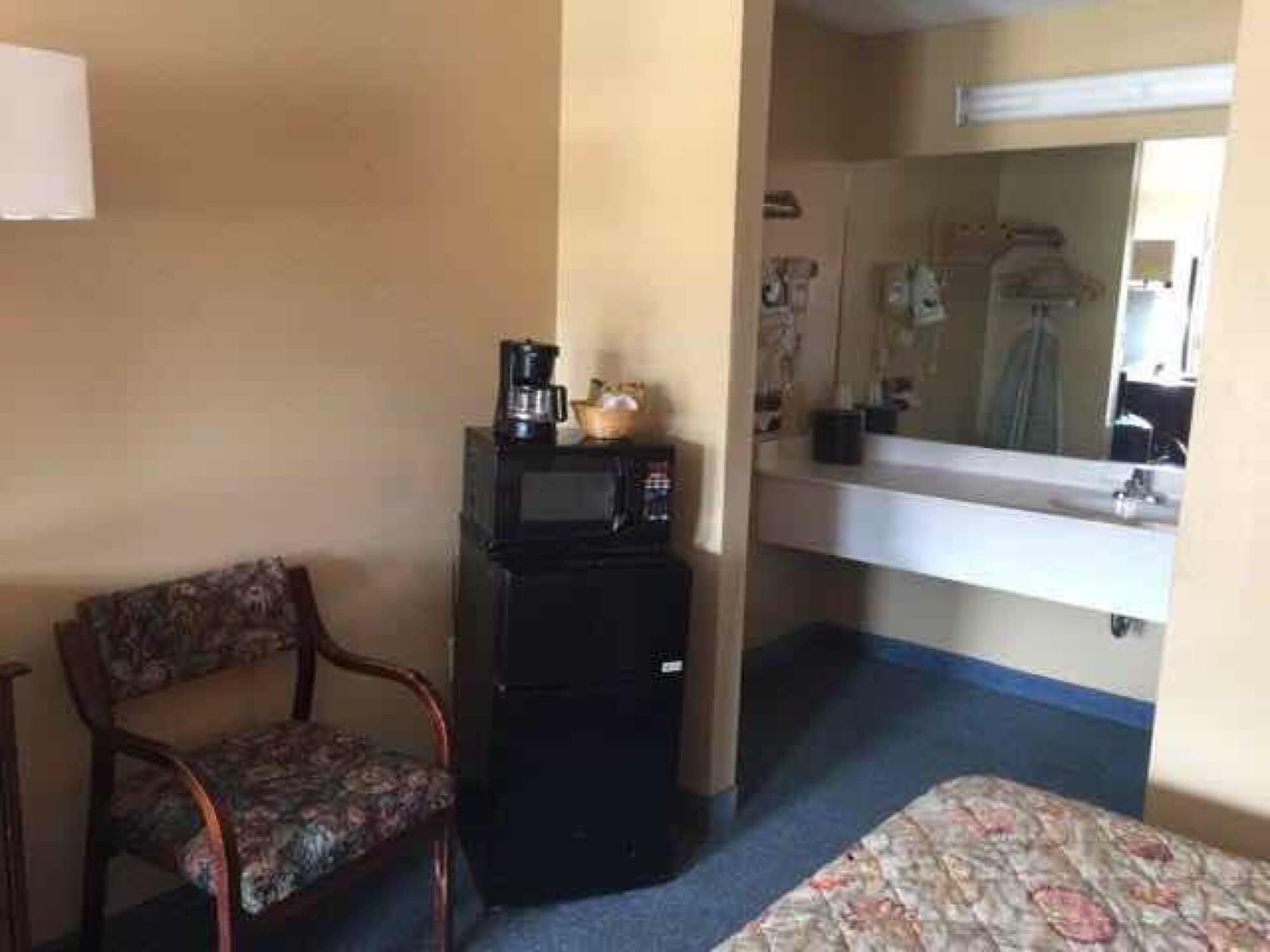 A small hotel room with a single bed, a chair, a microwave, and a sink with a mirror above it.
