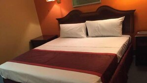 A neatly made bed with a white and red bedspread, a wooden headboard, and a nightstand with a lamp. - Motel 6 Bracey, VA – I-85 (Bracey)