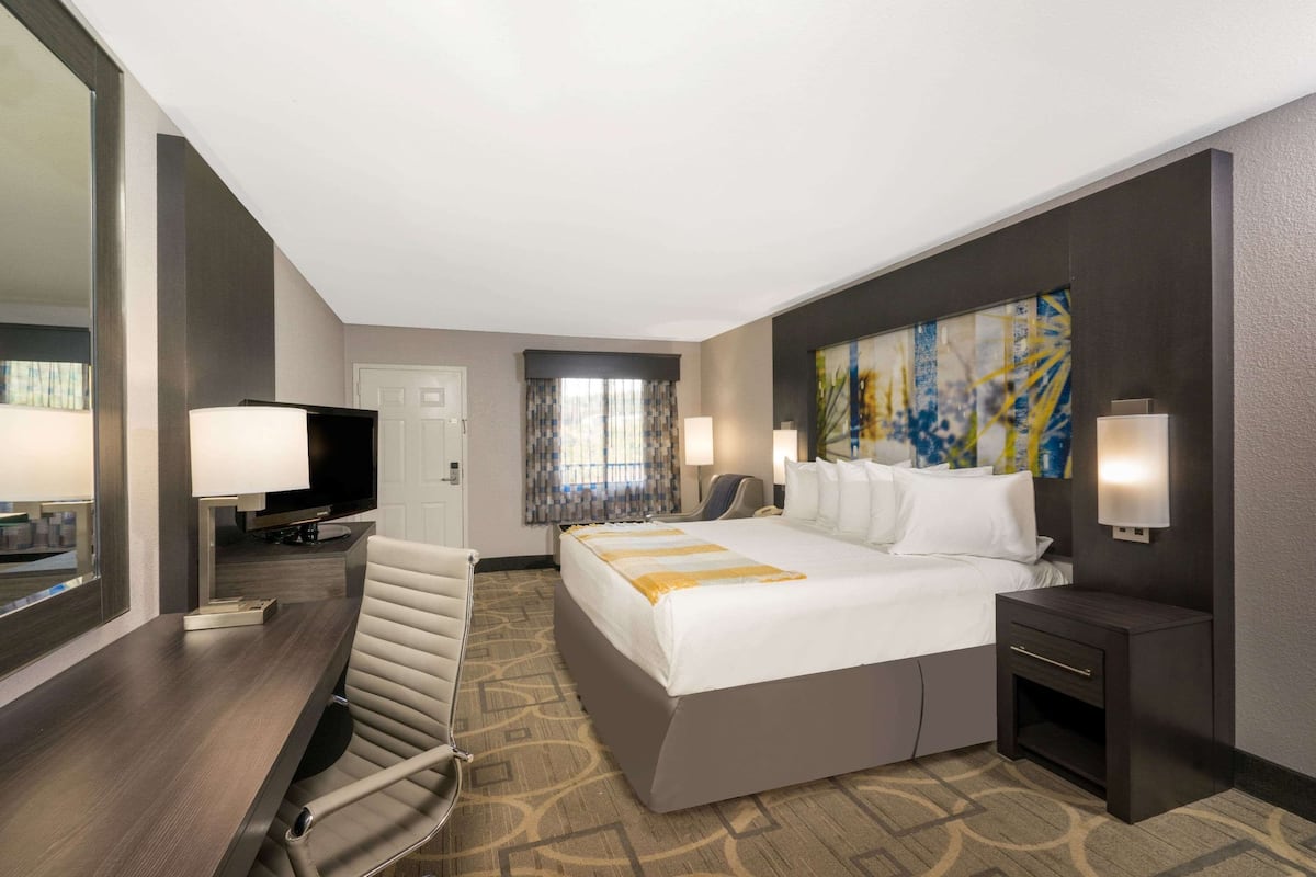 A hotel room with a large bed, a desk with a TV, a chair, a desk lamp, and a painting on the wall.