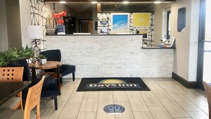 A reception area with a reception desk, a seating area with chairs and a table, a decorative wall, and a doormat with the hotel name.