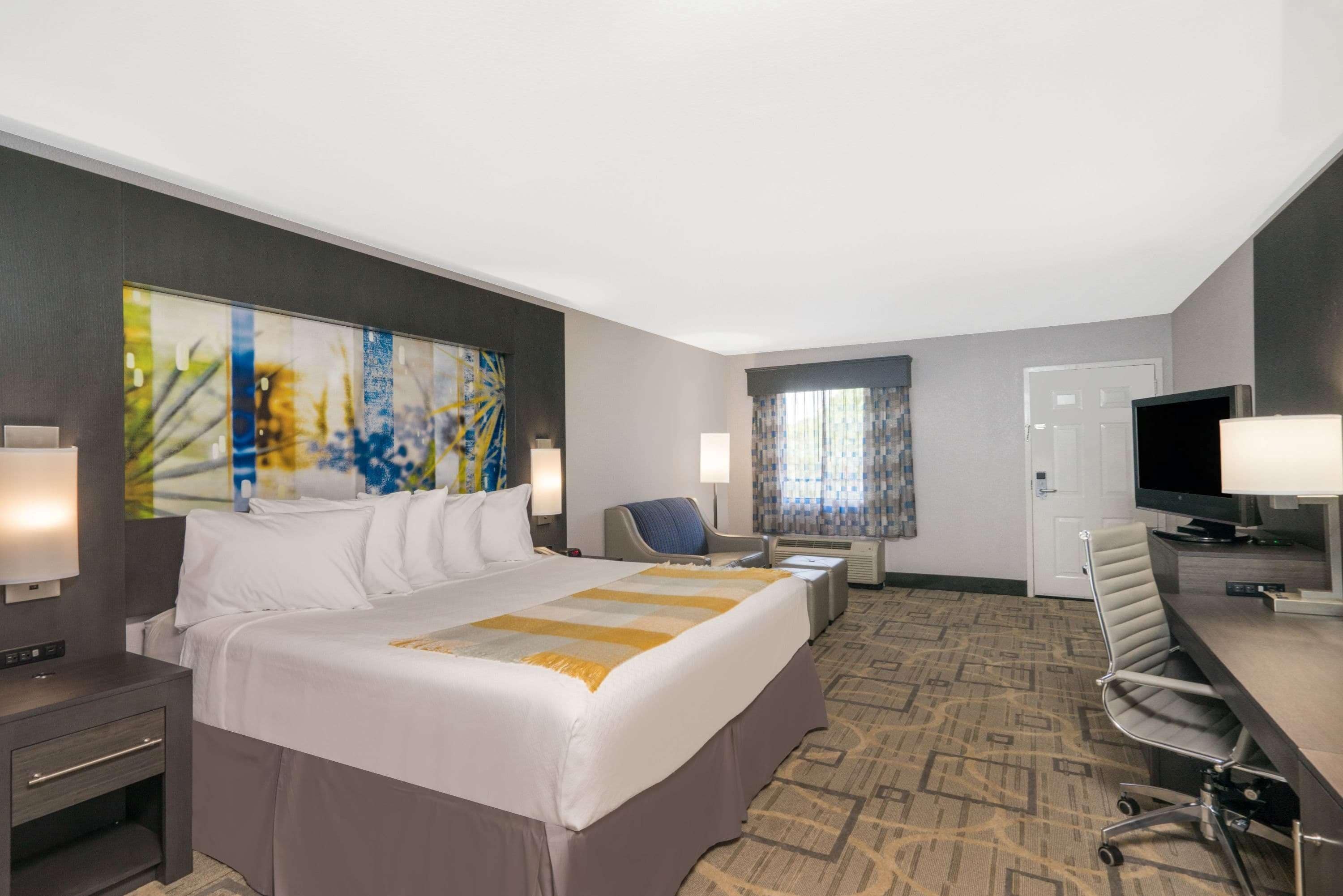A hotel room with a large bed, a desk with a chair, a television, and a window with curtains.