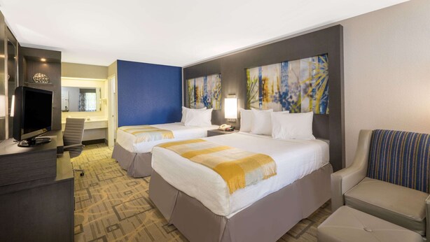 A hotel room with two beds, a desk, a TV, and artwork on the walls.
