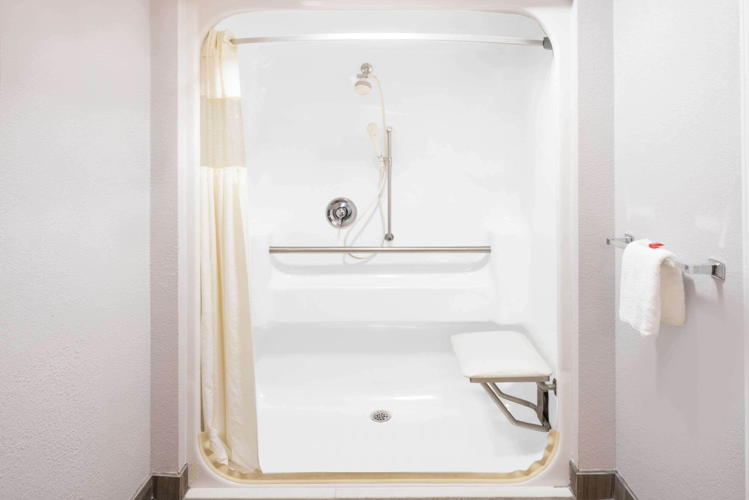 Une douche à l’italienne blanche, dotée d’un pommeau de douche à main, d’un flexible de douche et d’un petit banc.
