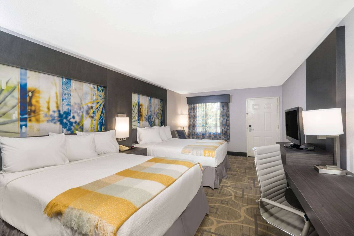 A hotel room with two beds, a desk, a TV, and artwork on the walls.