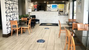 A restaurant with wooden chairs and tables, a reception desk, and a wall with a geometric pattern.