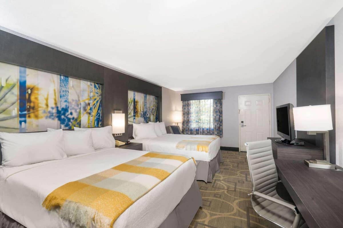 A hotel room with two beds, a desk, a TV, and artwork on the walls.