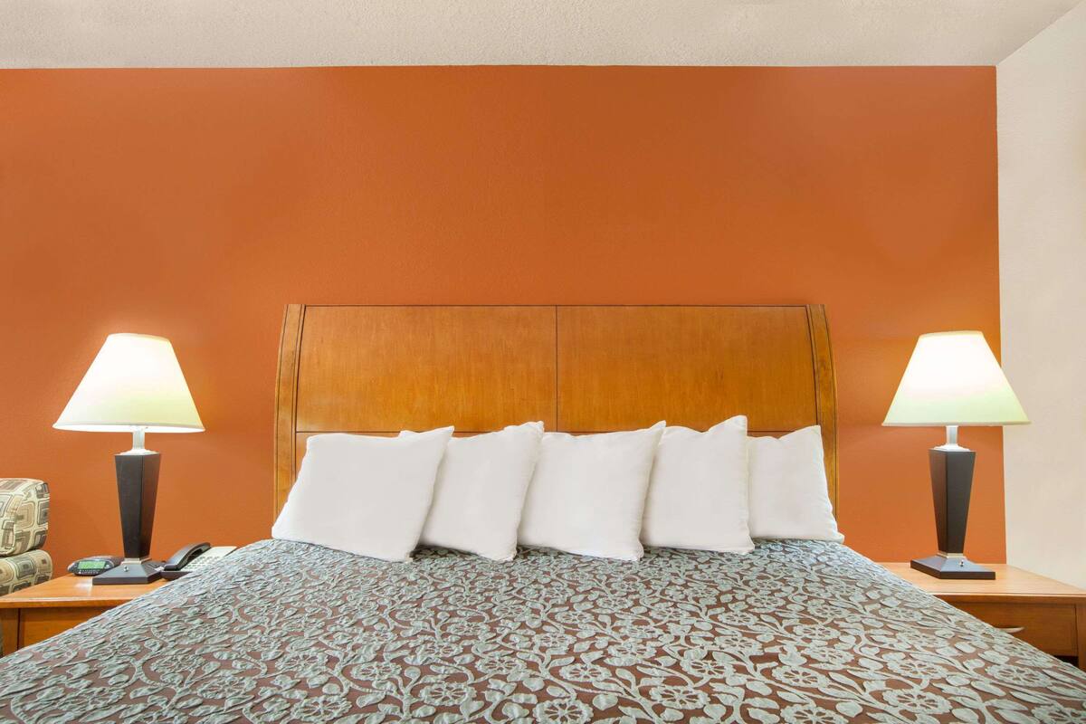 Habitación de hotel con cabecera de madera, colcha estampada, almohadas blancas y dos lámparas de noche.