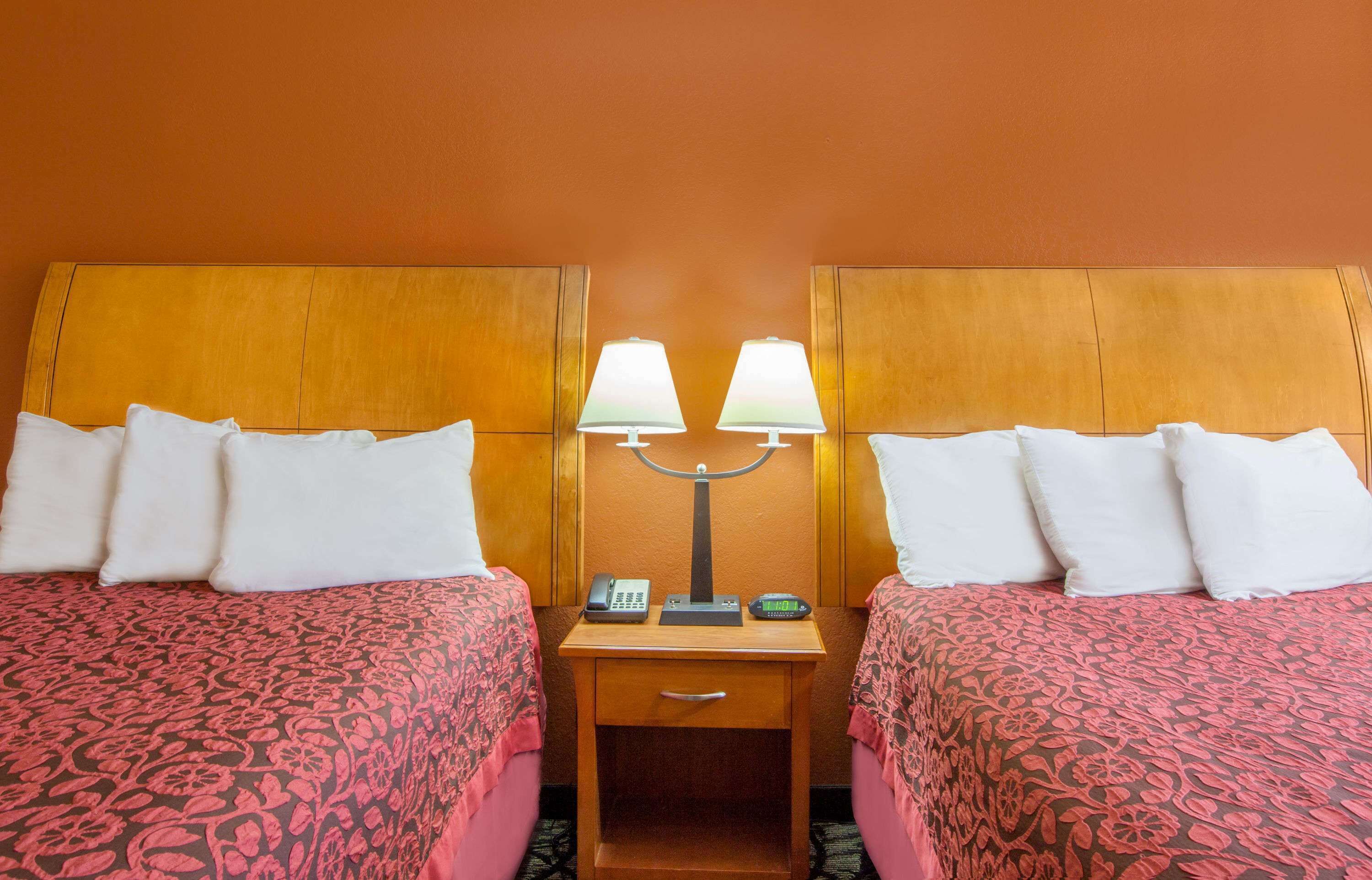 Ein Hotelzimmer mit zwei Betten, jeweils mit einem gemusterten Überwurf, einem Nachttisch mit Lampe, Telefon und digitaler Uhr.
