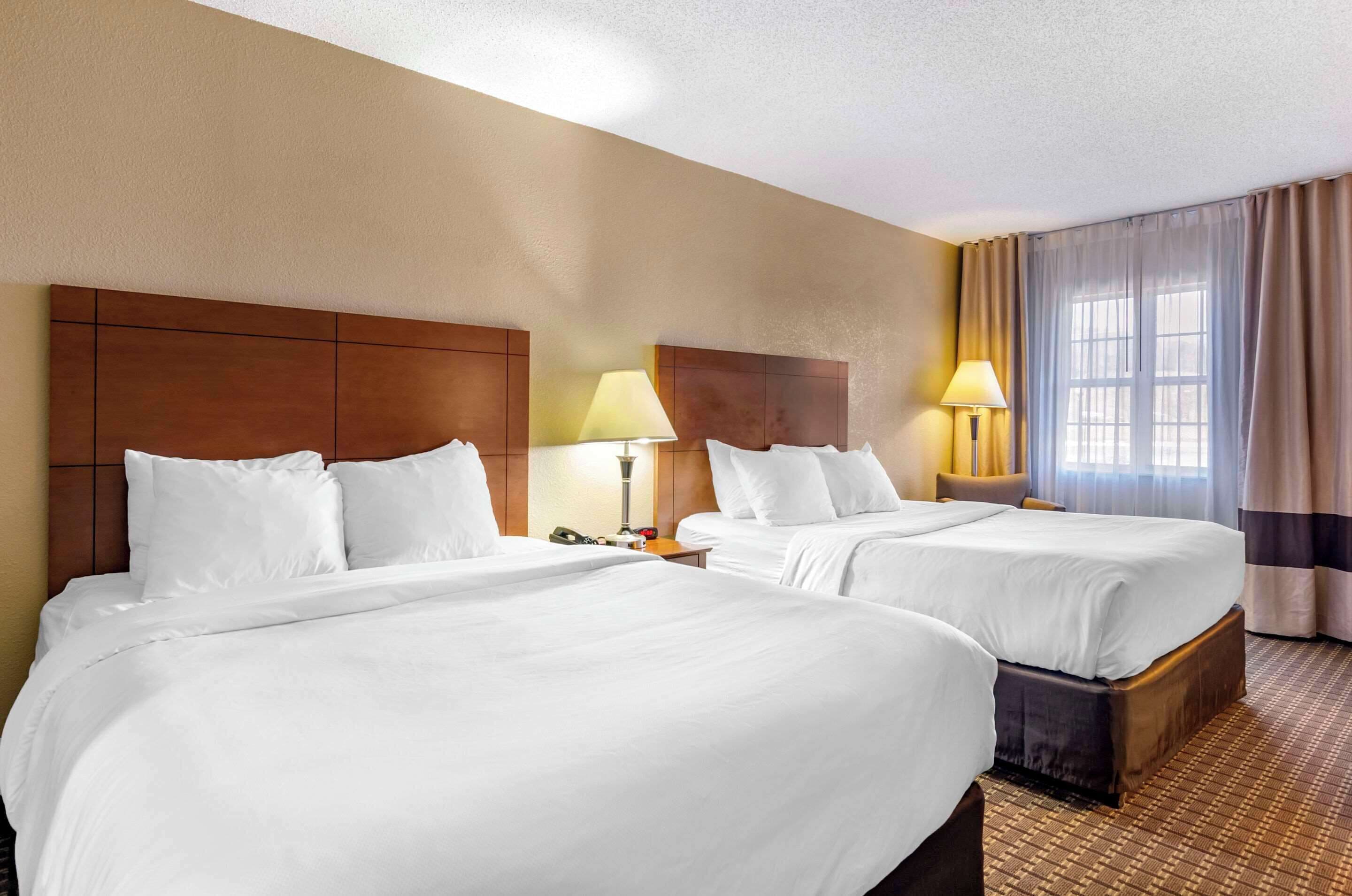 A hotel room with two beds, wooden headboards, bedside lamps, and a large window with curtains.