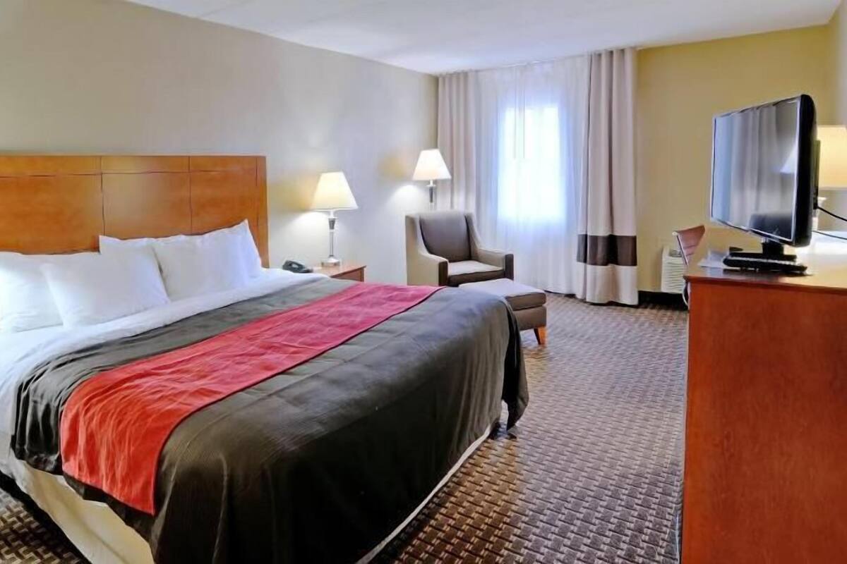 Une chambre d’hôtel comprenant un lit, deux lampes de chevet, une chaise, un bureau avec une télévision et une fenêtre avec des rideaux.