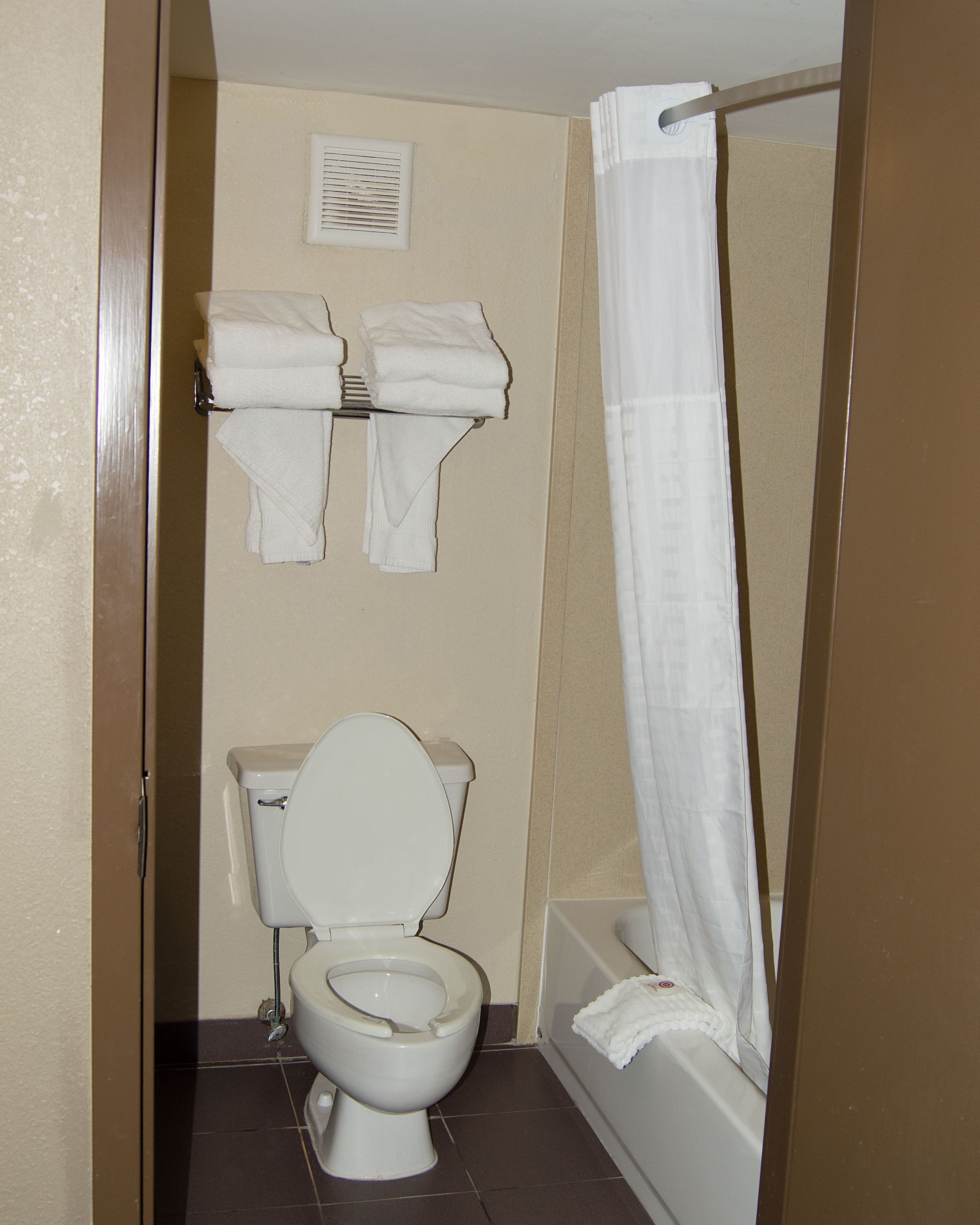 A bathroom with a toilet, a shower curtain, and a towel rack with towels.