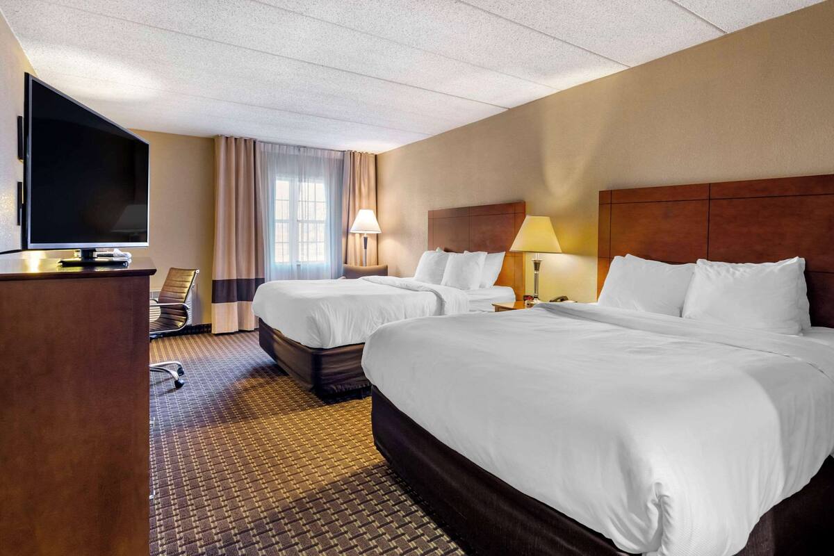 Une chambre d’hôtel avec deux lits, un téléviseur à écran plat, un bureau et une lampe.