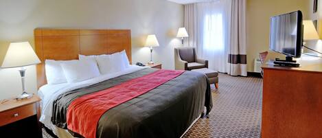 Hotelkamer met een groot bed, twee nachtkastjes met lampen, een stoel, een bureau met een televisie en een raam met gordijnen.