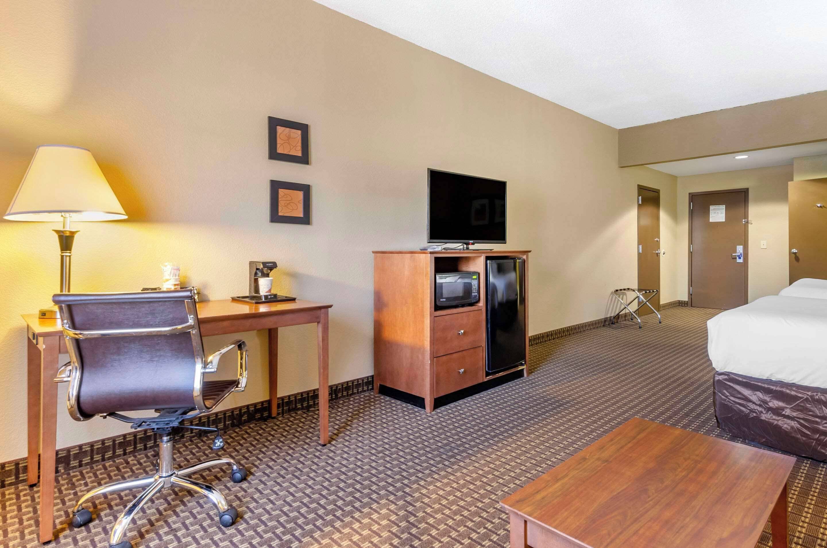 Habitación de hotel con escritorio, silla, televisión, microondas, refrigerador y una cama.