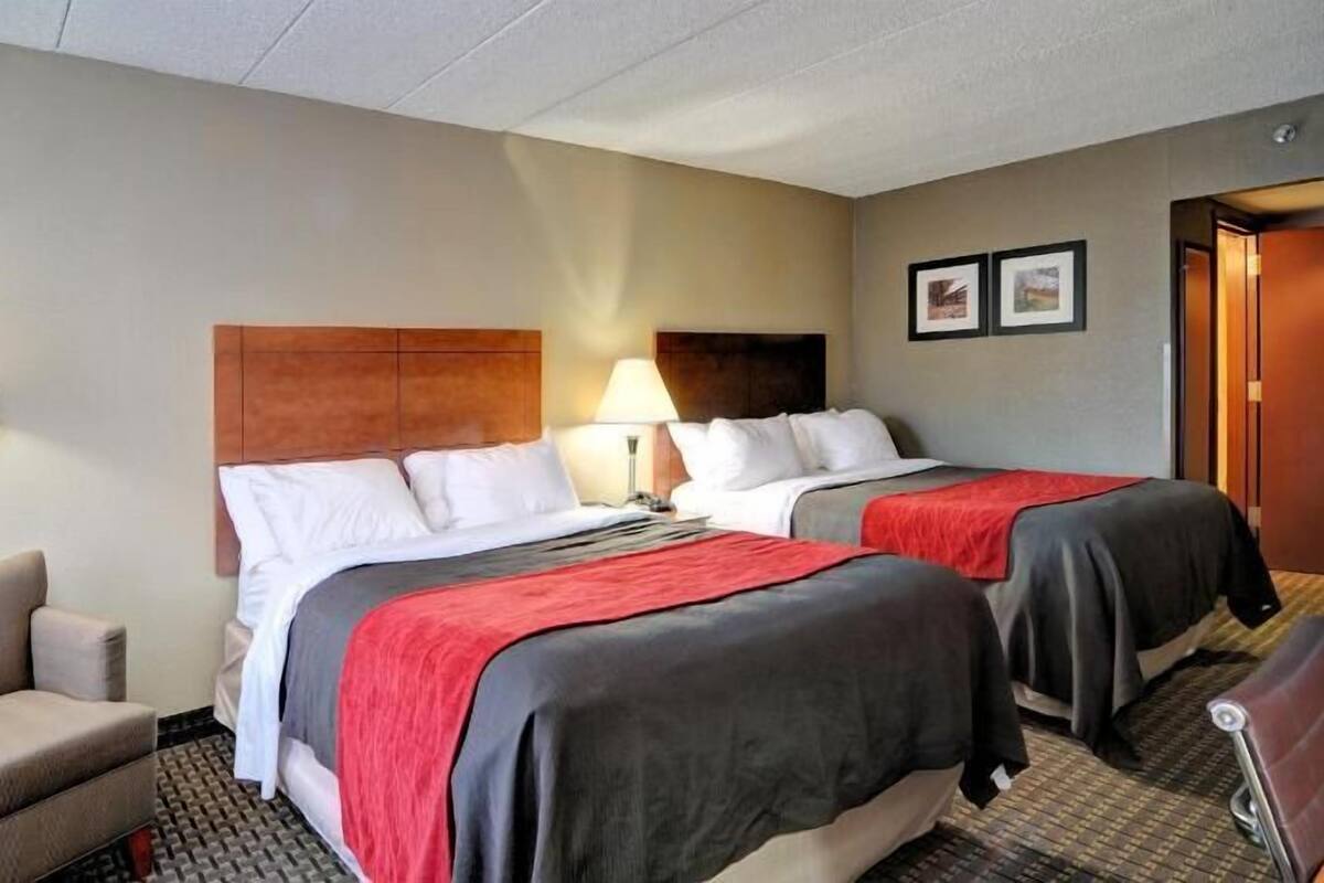 Une chambre d’hôtel avec deux lits, une chaise, une lampe et une porte.