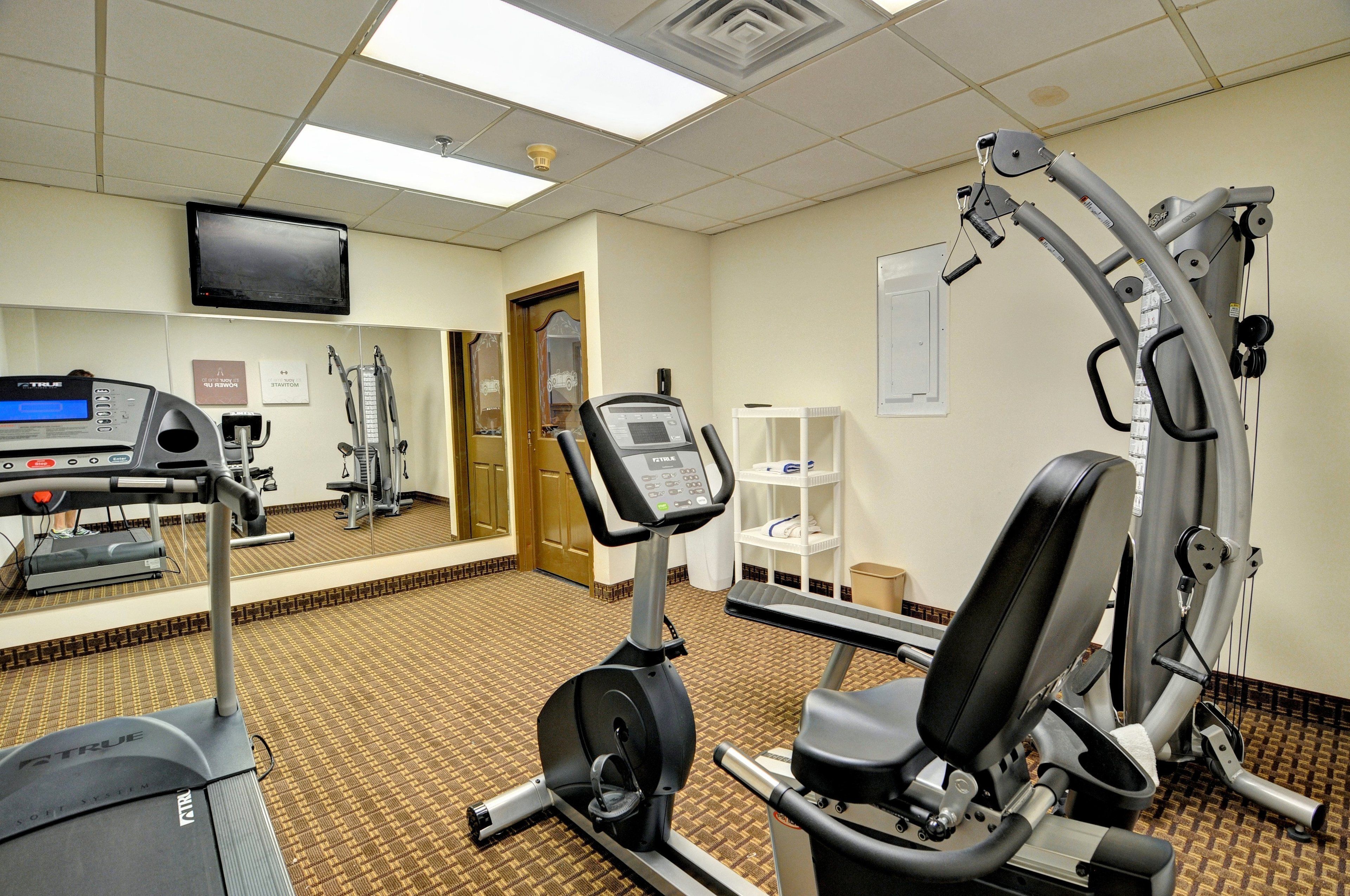 Un gimnasio de hotel con máquinas de cardio, un televisor y un espejo.