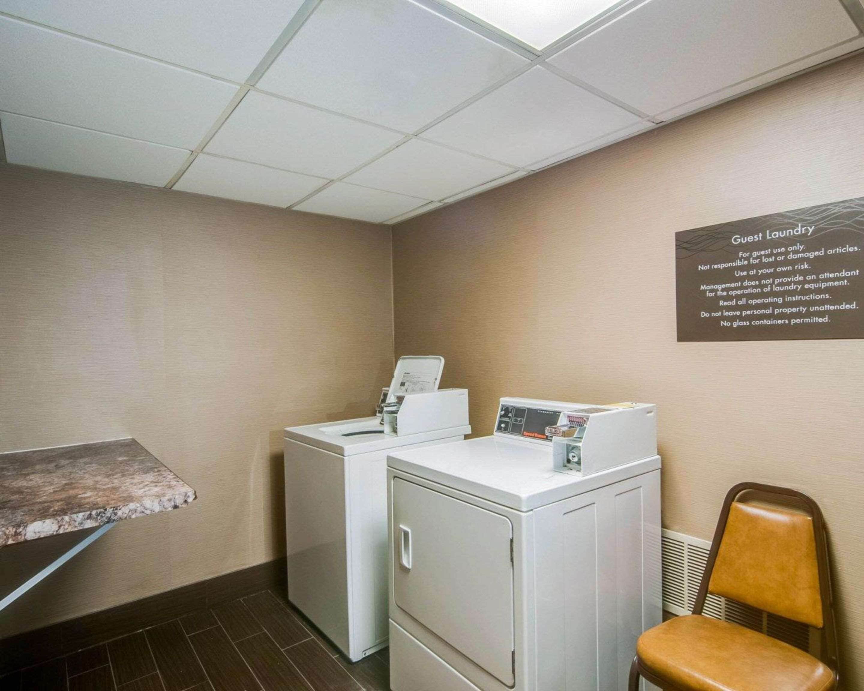 A laundry area with two washing machines, a chair, and a table. A sign on the wall provides laundry instructions.