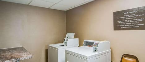 A laundry area with two washing machines, a chair, and a table. A sign on the wall provides laundry instructions.