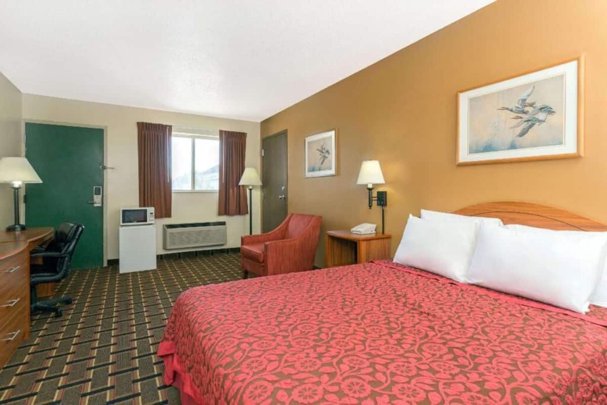 A hotel room with a bed, desk, chair, and artwork on the walls.