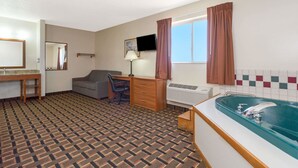 A hotel room with a patterned carpet, a desk with a chair, a television, a large window with curtains, and a bathtub. - Days Inn by Wyndham Paxton (Paxton)