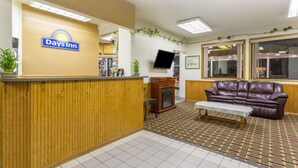 A reception area with a Days Inn sign, a wooden reception desk, a leather couch, a small table, and a patterned carpet. - Days Inn by Wyndham Paxton (Paxton)