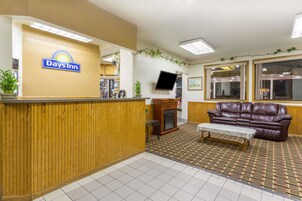 Zona de recepción con letrero de Days Inn, mostrador de madera, sofá de cuero, una mesita y alfombra estampada.