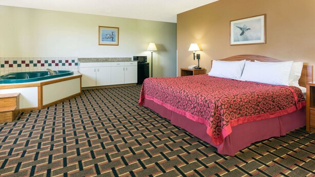 A hotel room with a bed, a desk with a sink, and a patterned carpet. - Days Inn by Wyndham Paxton (Paxton)