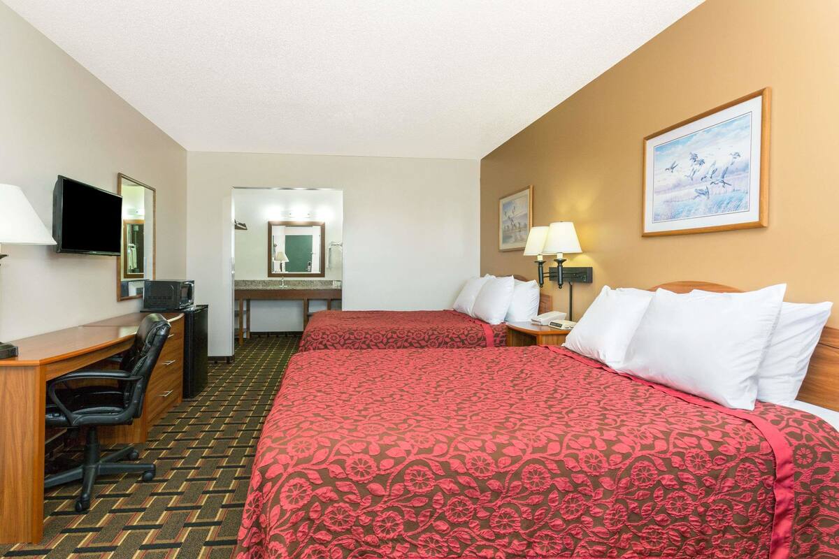 A hotel room with two beds, a desk, a chair, a television, and a framed picture on the wall.