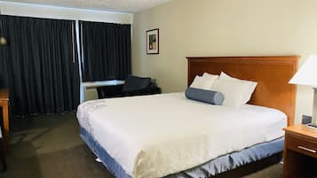 Una habitación de hotel con una cama grande, un escritorio, una silla y una ventana con cortinas.