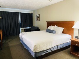 Una habitación de hotel con una cama grande, un escritorio, una silla y una ventana con cortinas.