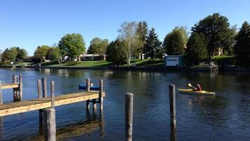 Un lago tranquilo con un muelle de madera que se adentra en el agua. Hay kayaks flotando y un pequeño edificio en la orilla.