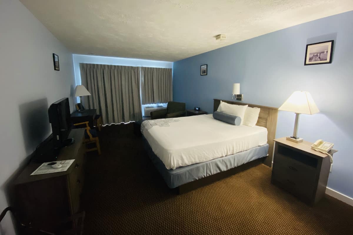 A hotel room with a bed, a desk with a computer, a chair, a lamp, and a telephone.