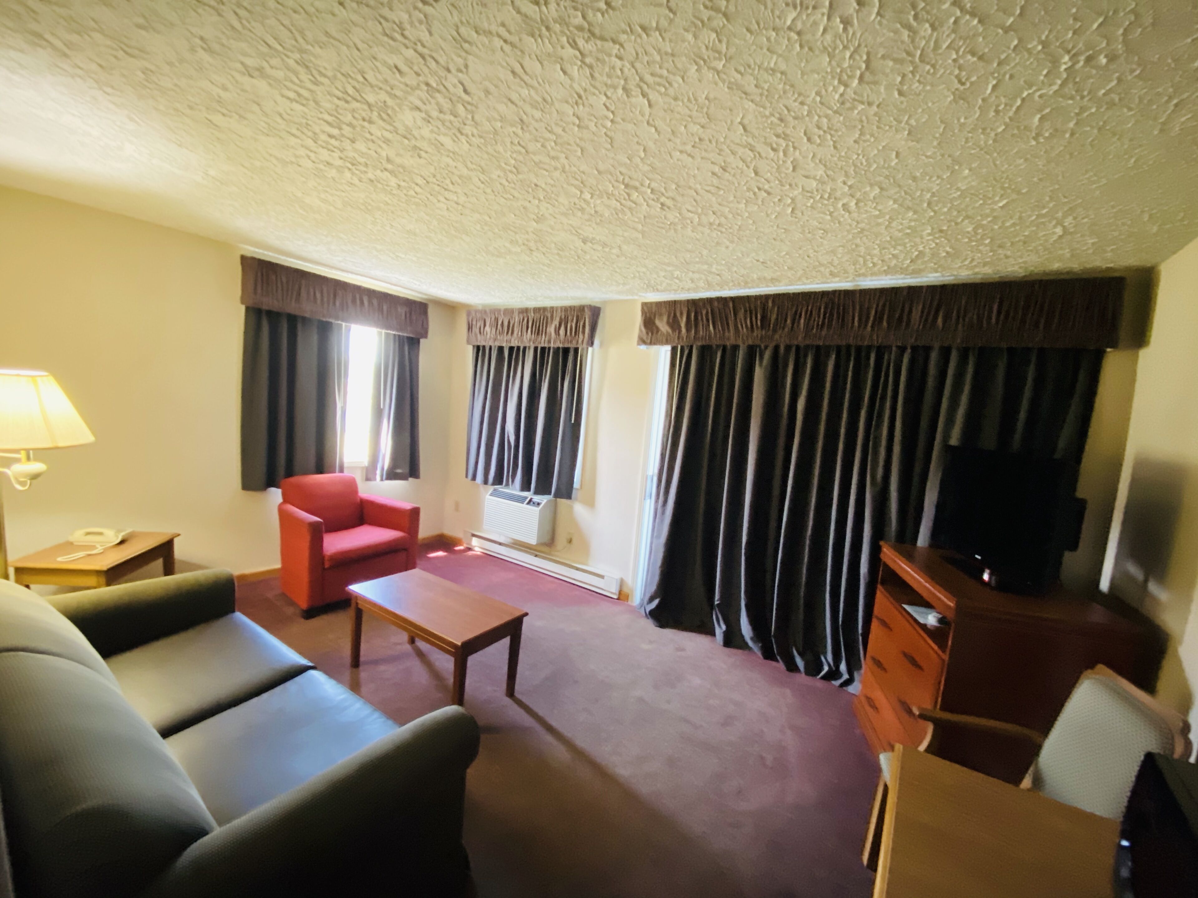 A hotel room with a sofa, armchair, coffee table, and a TV on a wooden cabinet.