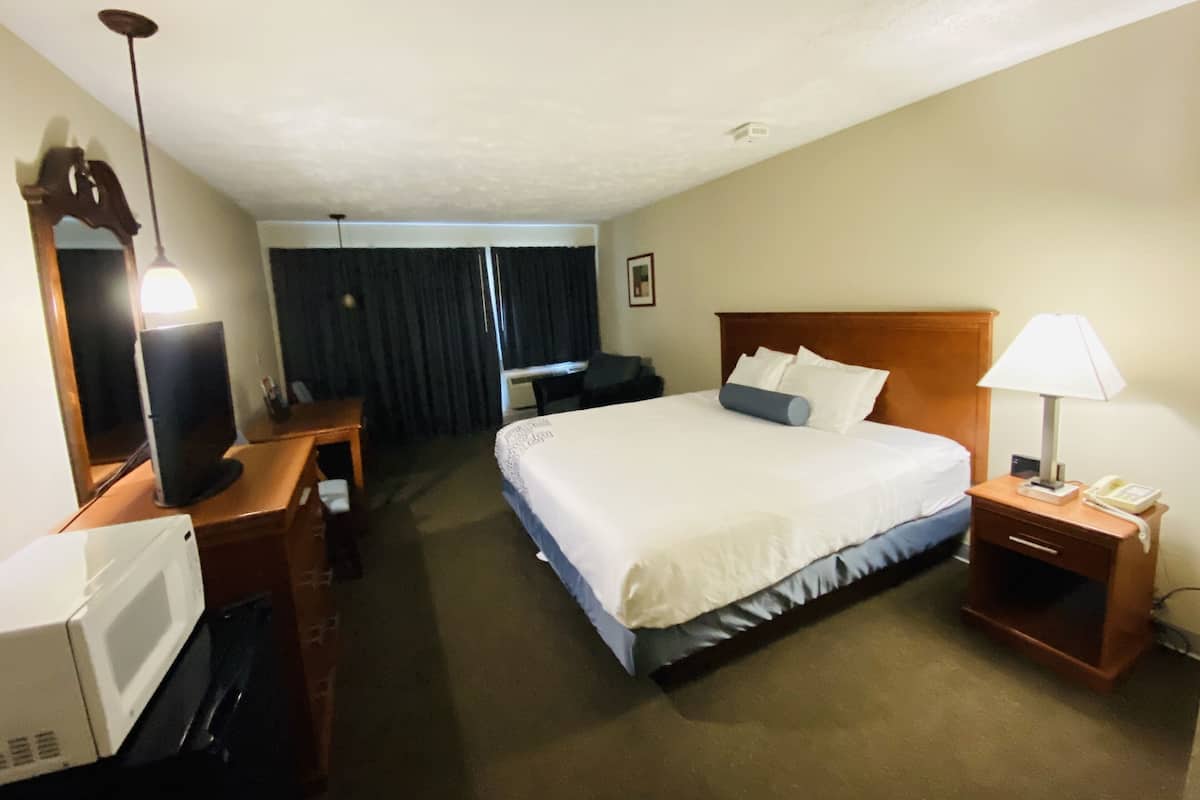 A hotel room with a bed, a desk with a computer, a lamp, and a telephone.